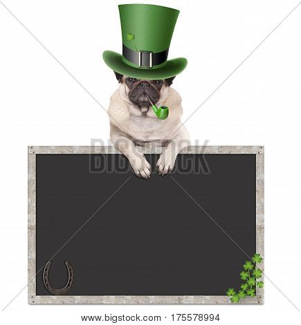 lovely cute pug puppy dog with leprechaun hat for st. patrick's day smoking pipe leaning on blank chalkboard sign with horseshoe and shamrock isolated on white background