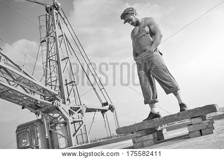 Time to think. Monochrome low angle shot of a thoughtful young muscular male builder dressed in vintage clothes standing on the roof of a building people retro profession worker crane concept