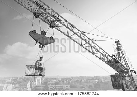 Extreme lunch. Black and white shot of an old fashioned shirtless relaxed construction worker having lunch sitting on a crossbar hanging from the crane high above the city.