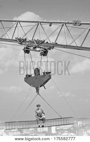 Vertical monochrome shot of a shirtless retro styled construction worker enjoying lunch sitting high above the city on a metal crossbar.