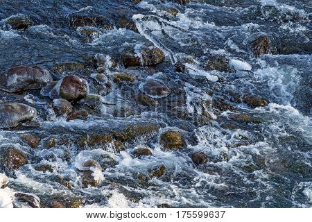 Raging water breaker among icy rocks with frazil of mountain river in winter