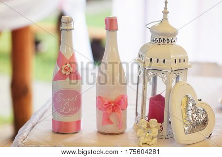 Champagne In White Bottles Stand Behind A  White Lantern With Red Candle