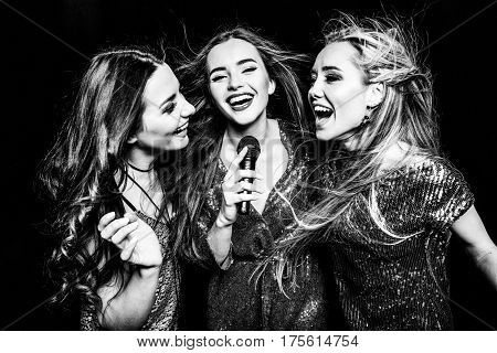 Black and white photo of three gorgeous women in festive dresses singing karaoke