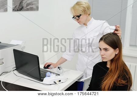 Doctor examines the hairy part of the patient's head - pretty young girl. Trihoskopiya, psoriasis, dandruff, split ends, peeling, dermatology.