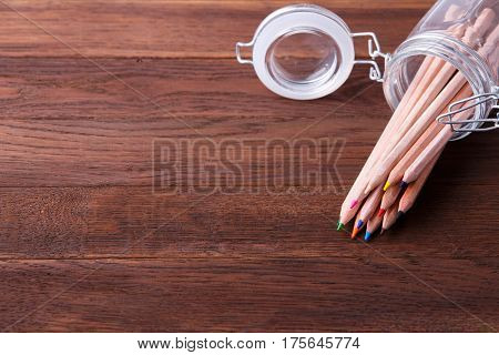 Set of coloured pencils in a glass pot on a wooden table. Brown background. NAtural materials. Drawing and painting. School and education. Artist.
