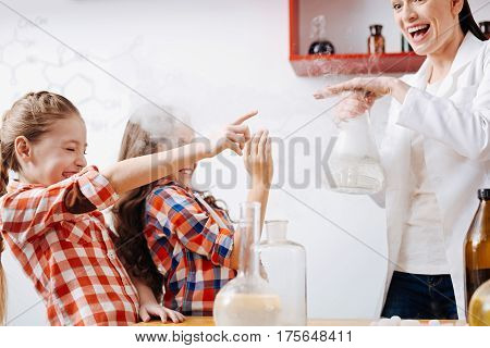 Positive emotions. Cute delighted positive girls closing their eyes and trying to touch a chemical flask while enjoying their time in the lab