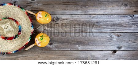 Flat lay view of yellow maracas and large sombrero on rustic red wooden boards for Cinco de Mayo concept. Plenty of copy space.