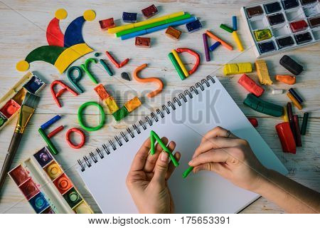 hands make April Fools' Day text made with plasticine on white wooden background
