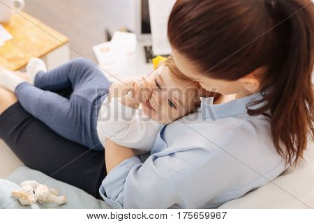 My sunshine. Delicate loving modern mom hugging her child while taking some time off her work and enjoying every minute of it