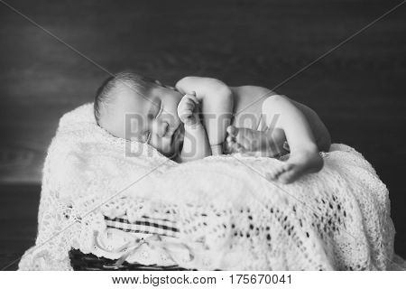 Adorable beautiful newborn baby girl. One week old newborn baby sleeping in basket. Black and white photo. Dark wooden background