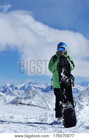 snowboarder standing with snowboard in the mountains. Beautiful winter landscape with ridge, blue sky in the background. Photo on a theme of extreme sports, winter sports, snowboarding.