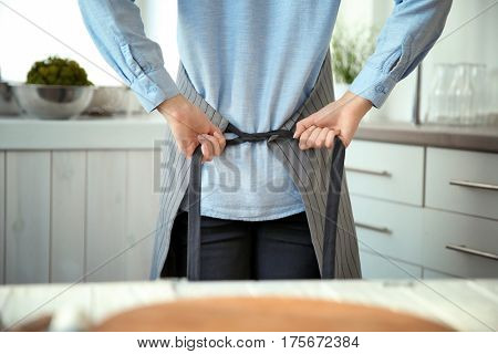 Woman tying up her apron around the waist in kitchen
