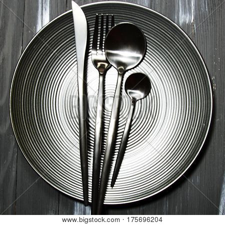 A black plate with cutlery on a wooden background with copy space top view.