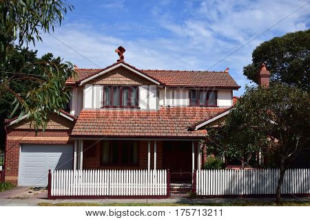 suburban house with red tiled roof and white picket fence on sunny day