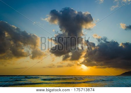 Sunrise over the sea, the rolling calm waves,  horizon is orange, skay orange and blue, clouds are grey and pink.