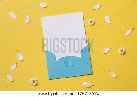 Spring or summer background with copy space for text: blank stationary template / invitation mockup in cyan envelope with butterfly chamomiles and petals. Top view. Flat lay.