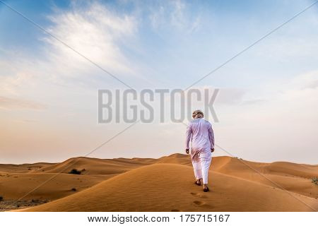 Arabian man walking in the desert at sunrise