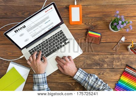 Person working on Computer on cozy dark wooden Table with clear Wood texture with Computer and other Electronic and Lifestyle Gadgets and Flower on Desk top View.