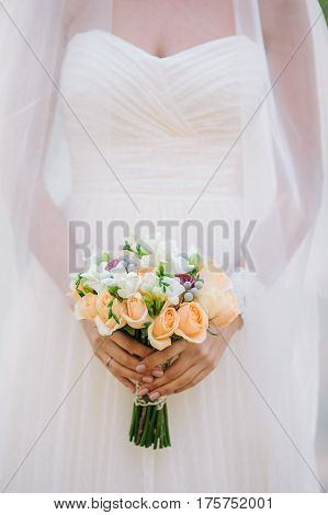 Beautiful woman in a white wedding dress holding a flowers bouquet from rose in hand outside. Wedding bridal bouquet.