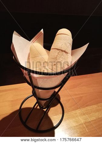 French bread mini baguette as side dish serve in paper on holding tray on wood table focus-on-foreground with isolate black background