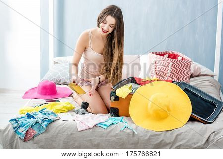Young woman packing clothes to the suitcase sitting on the bed. Prepairing for the summer vacations