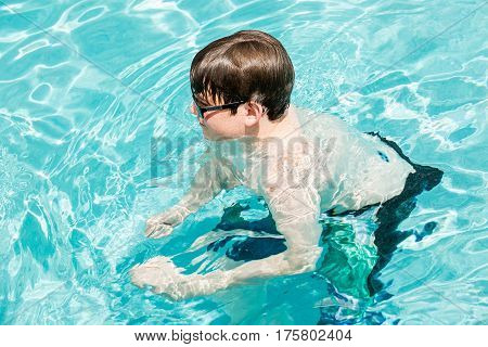 Teenager boy faving fun in outdoor swimming pool on hot summer day.