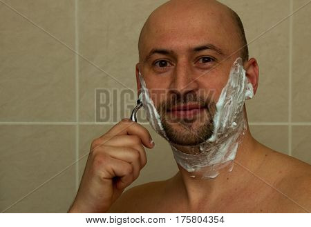 Man shaving his face with the razor blade through shave foam. Men skin care concept. Bald