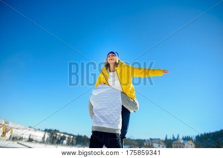 Young man holding in his arms his girlfriend. Man sturdily built easily picks up a fragile girl. Young people having fun. Against the background of the blue sky.