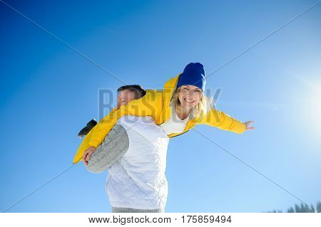 Young man holding in his arms his girlfriend. Man sturdily built easily picks up a fragile girl. Young people having fun. Against the background of the blue sky.