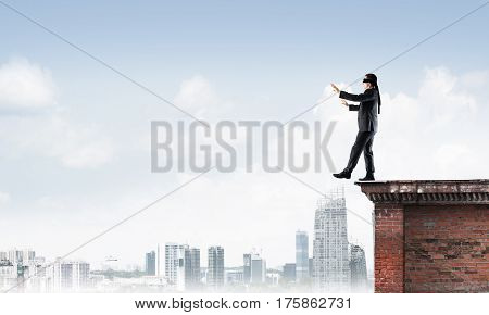 Businessman with blindfolder on eyes walking on building top
