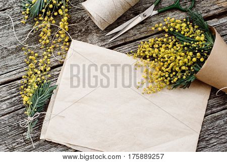 Make bouquet of mimosa. bandages twine and scissors on rustic wooden table, old paper for text. Copy space for text. top view