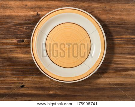 Orange round plate is photographed top view on a background of old wood table planks. Ceramic plate with round pattern