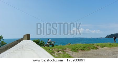 Mount Maunganui, New Zealand - February 28, 2017; Couple sitting on seat on other side wooden fence on Mount base track looking out to sea Mount Maunganui New Zealand.