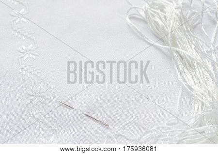 Texture of linen fabric with embroidery by flat stitch. Needle and white silk threads. Macro handmade embroidery.