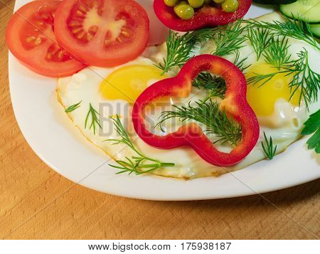 Fried egg decorated with red sweet red pepper and wedges of juicy tomato on a snow-white plate. An example of the correct serving.