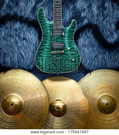 Turquoise electric guitar with three cymbals on blue faux fur wall. Musical instruments background
