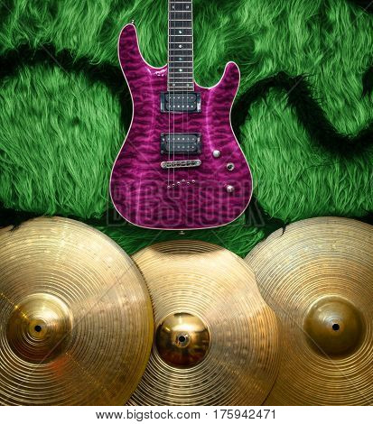 Purple electric guitar with three cymbals on green faux fur wall. Musical instruments background