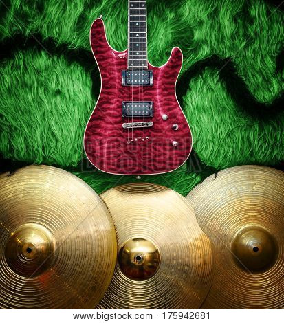 Red Electric guitar with three cymbals on green faux fur wall. Musical instruments background