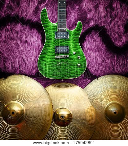 Green electric guitar with three cymbals on faux fur wall. Musical instruments background