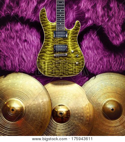 Yellow electric guitar with three cymbals on pink faux fur wall. Musical instruments background