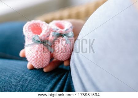 future mother knows a sex of her baby. Pregnant woman holding pink knitted baby bootees at a stomach with selective focus.