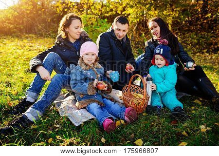 Happy Young Family Of Four Having Picnic At Meadow At Summer Day