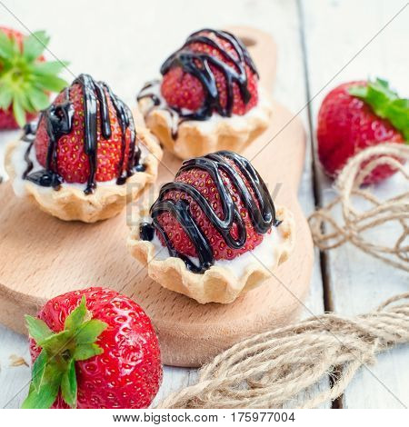 Strawberry cake with vanilla cream on white rusric wooden background. Sweet basket tartlet with strawberries and chocolate. Tasty summer dessert. Selective focus.