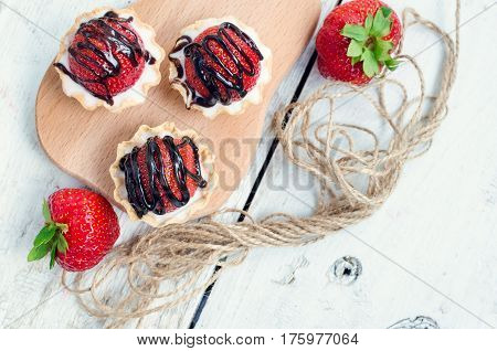 Strawberry cake with vanilla cream on white rusric wooden background. Sweet basket tartlet with strawberries and chocolate. Tasty summer dessert. Top view.