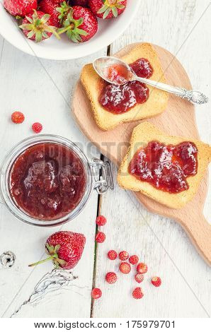 Toasts with strawberry jam for breakfast on white rusric wooden background. Top view.