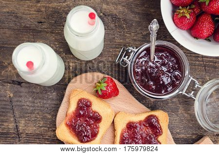 Toasts with strawberry jam and milk for breakfast on rusric wooden background. Top view.