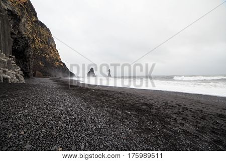 Beautiful volcanic black sand beach in Dyrholaey, Iceland. The rocky formations of the bottom, in the water, are considered by the Icelandic legends like "trolls" turned into stone.