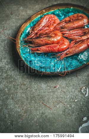 Raw uncooked red shrimps on chipped ice in turquoise blue ceramic tray over grey concrete background, copy space, vertical composition. Fresh seafood concept