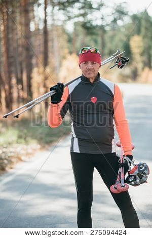 Training An Athlete On The Roller Skaters. Biathlon Ride On The Roller Skis With Ski Poles, In The H