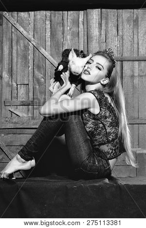 Elegant Stylish Young Woman In Thin Rim Holding Cute Little Pig In Hands In Fur Coat Indoor On Woode